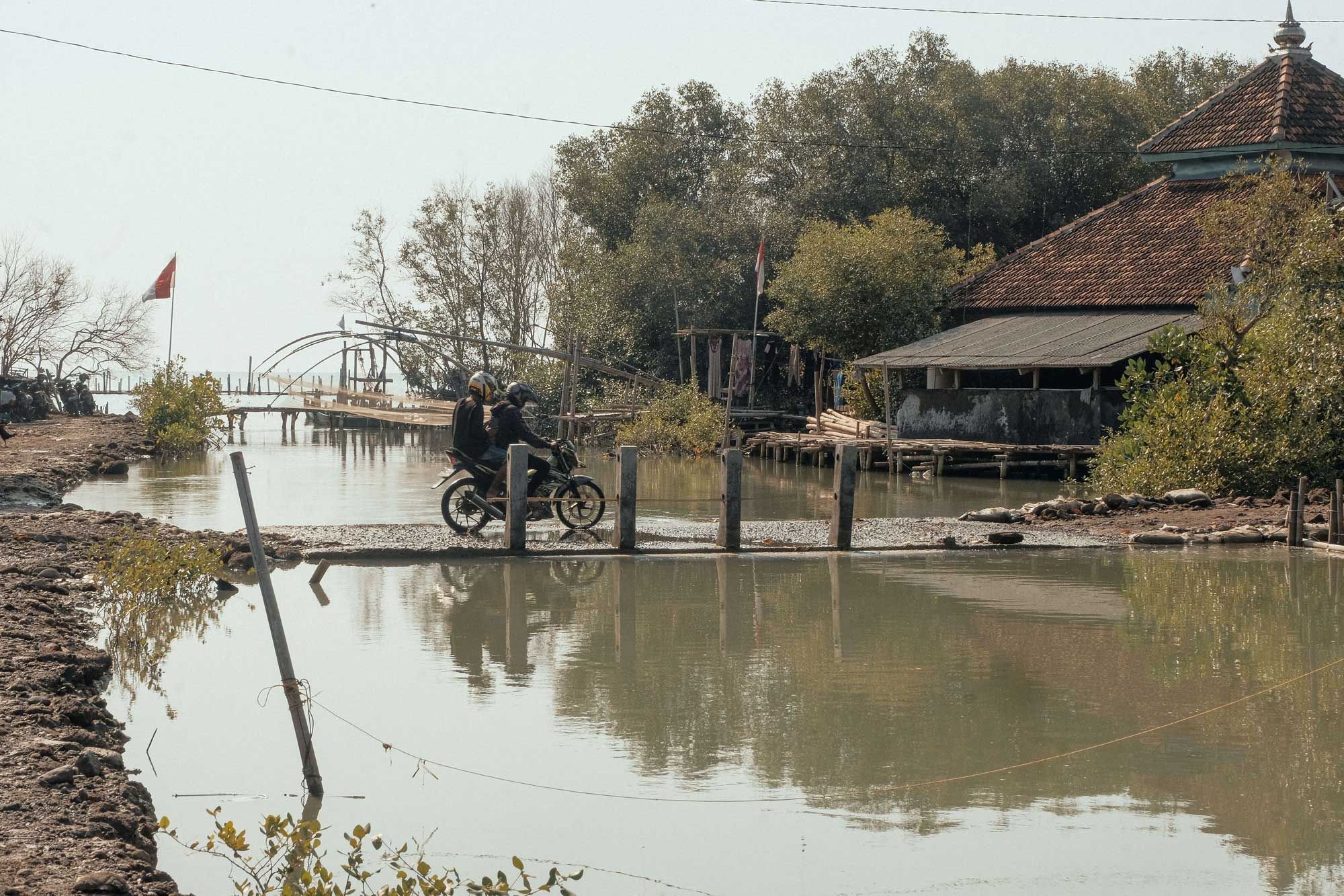 Two-people-on-a-motorcycle-crosses-a-narrow-bridge-as-residents-carry-on-with-daily-life-amid-rising-waters-and-sinking-land.-Photo-credit_-Kota-Kita_Angga-Bakti